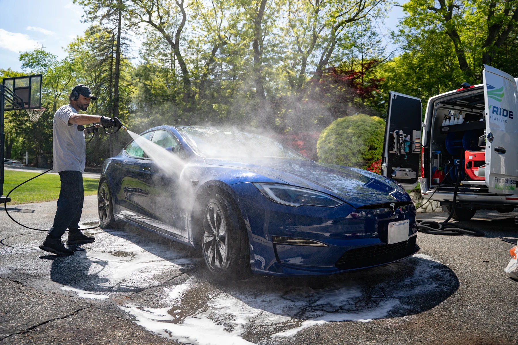 FlyMyRide technician rinsing a blue Tesla beside the equipped mobile service van